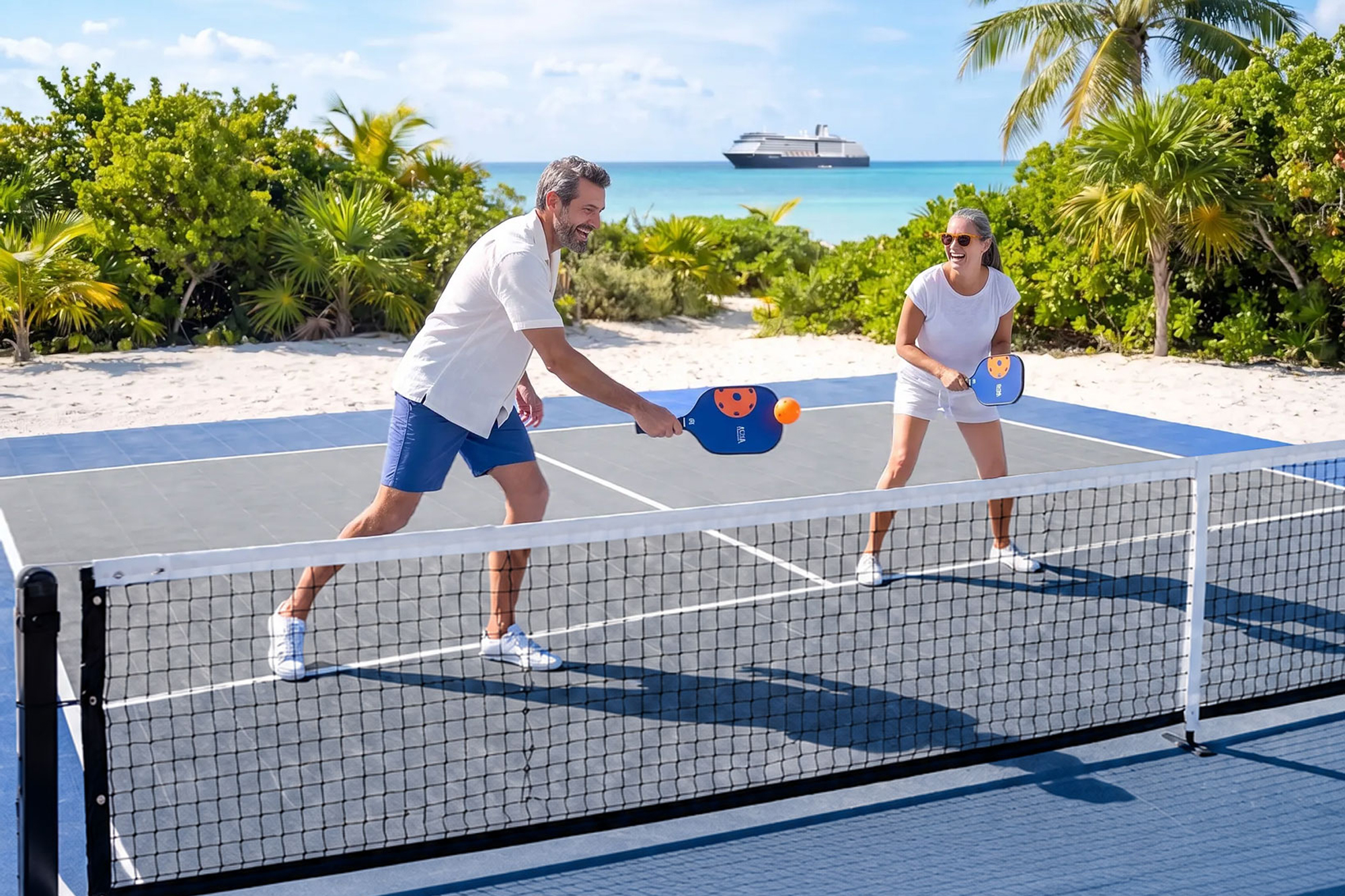 A couple playing pickleball on Half Moon Cay with a Holland America Line ship in the background